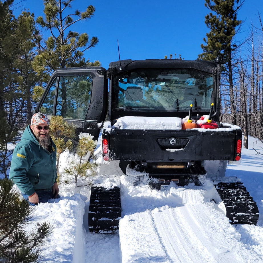 Person standing next to a snow-covered vehicle with tracks in a snowy landscape. Over the Top Intake installed. 